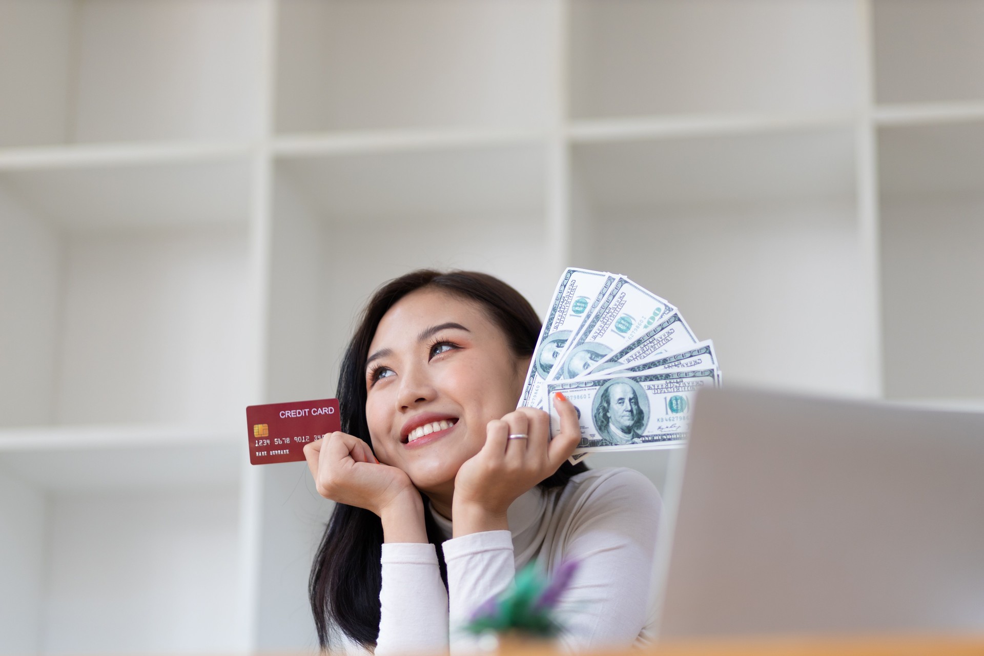 Cheerful happy Asian woman holding money and credit card.